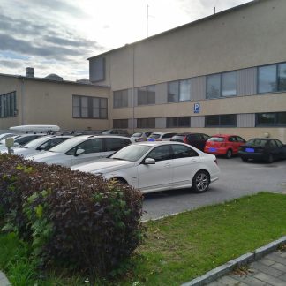 Useita autoja parkissa koulurakennuksen parkkipaikalla.