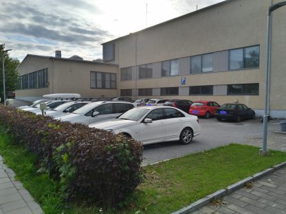 Useita autoja parkissa koulurakennuksen parkkipaikalla.